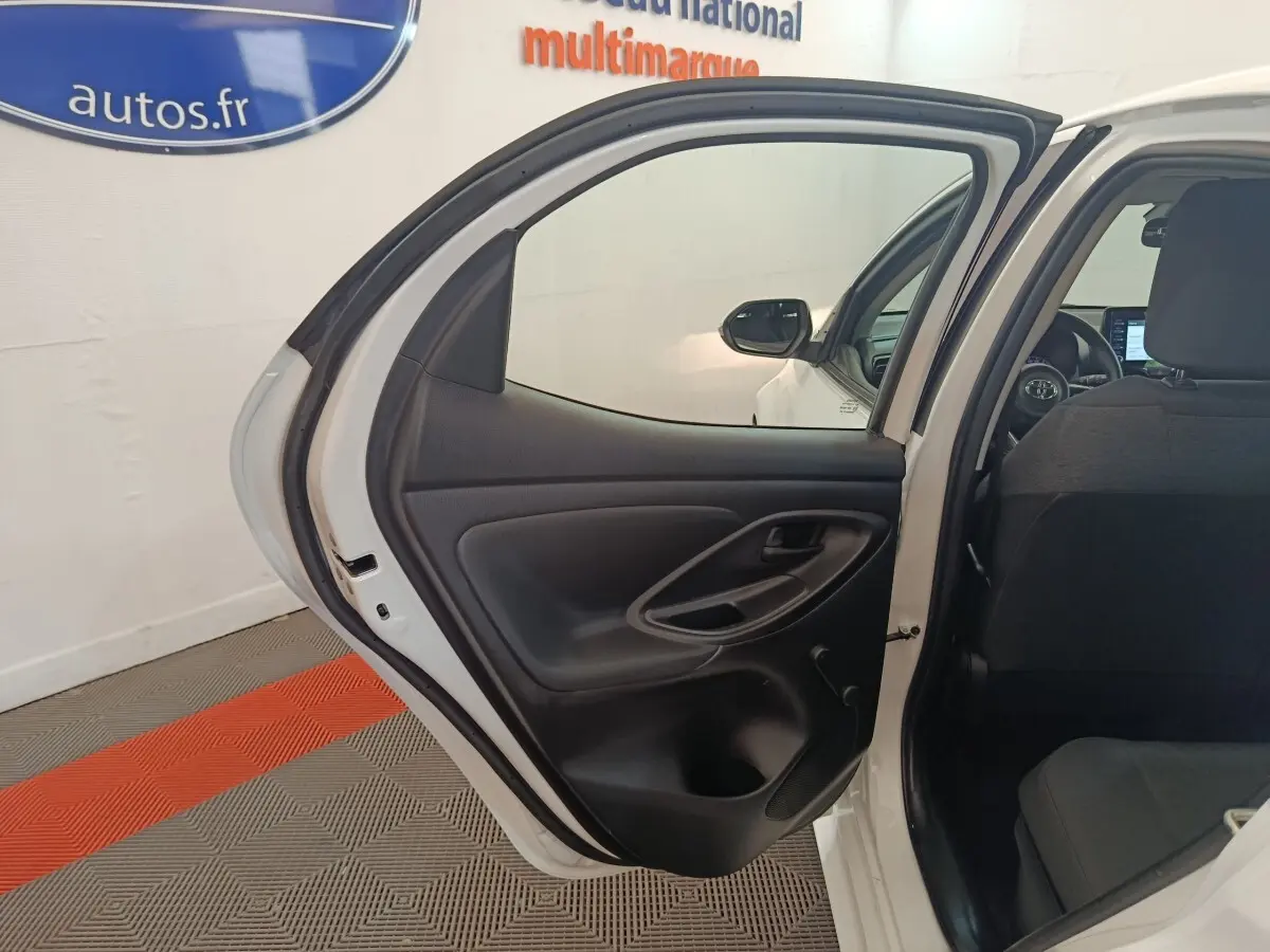 Vue intérieure sur la porte arrière gauche ouverte d'une Toyota Yaris blanche 2022, avec siège arrière et tableau de bord partiellement visibles.