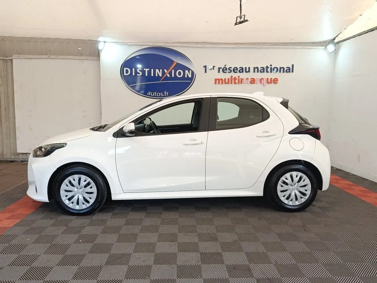 Toyota Yaris hybride blanche vue de profil côté gauche, avec jantes standard et spoiler arrière noir.
