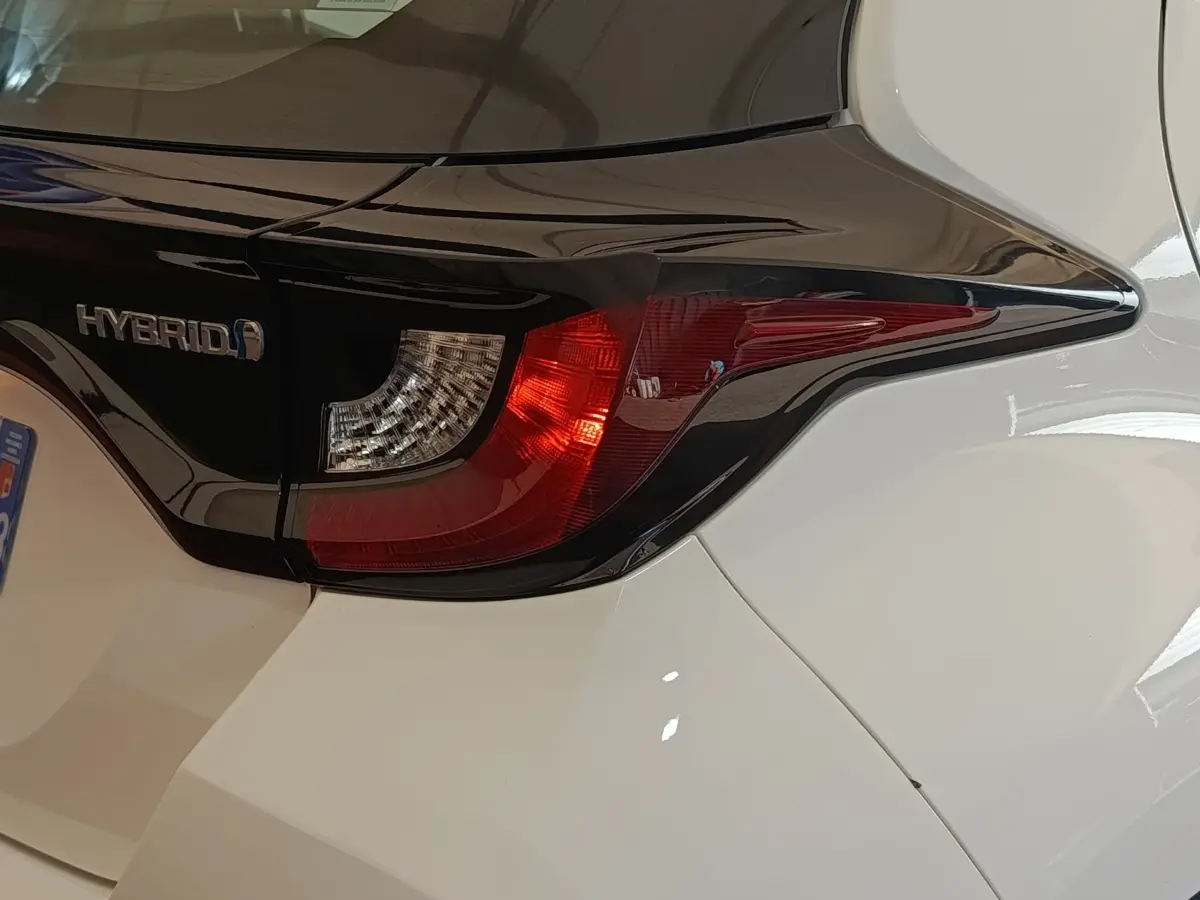 Gros plan sur le feu arrière droit noir et rouge d'une Toyota Yaris hybride blanche, avec logo Hybrid visible.