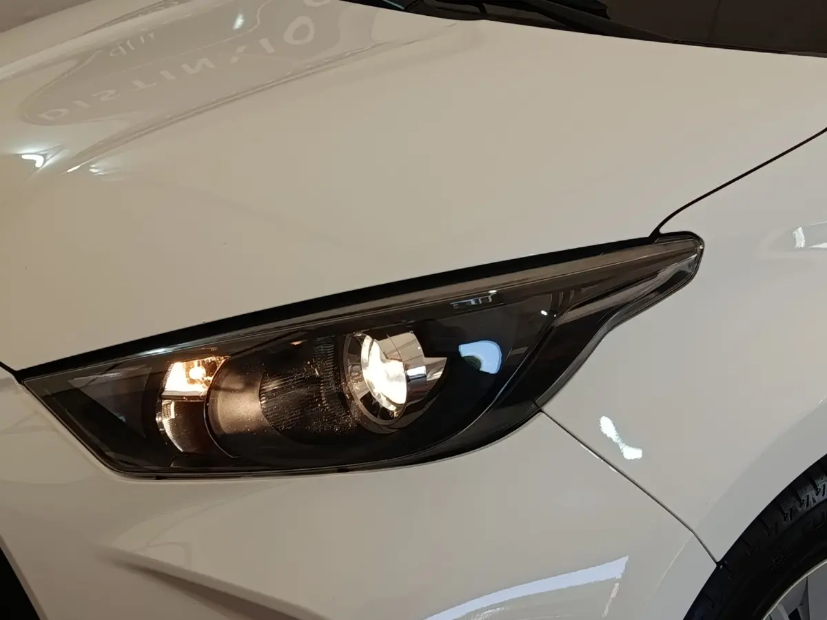 Gros plan sur le phare avant droit allumé d'une Toyota Yaris blanche, soulignant les lignes épurées du capot.