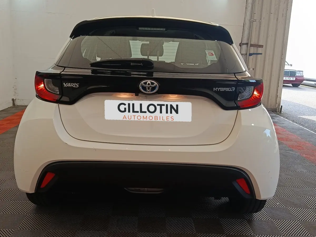 Vue arrière de la Toyota Yaris hybride blanche 2022 avec spoiler noir et feux arrière allumés dans un garage.