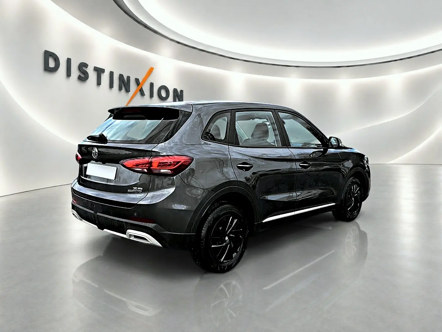 Vue 3/4 arrière droite du MG ZS Camden grey 2026 avec jantes noires et becquet arrière dans un showroom.
