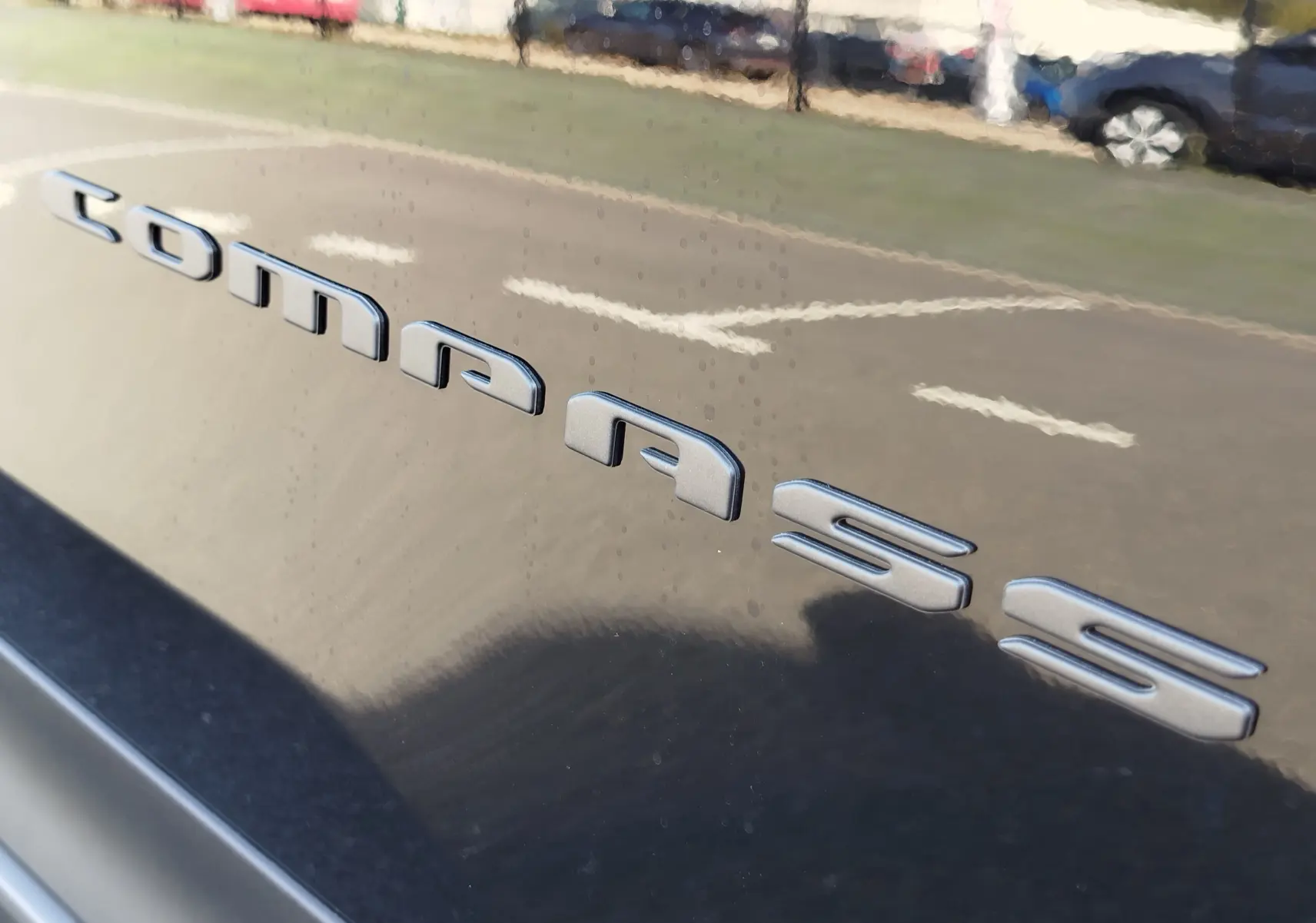Gros plan sur l’inscription "Compass" en relief sur la carrosserie noire Vulcano Metal d’un Jeep Compass.