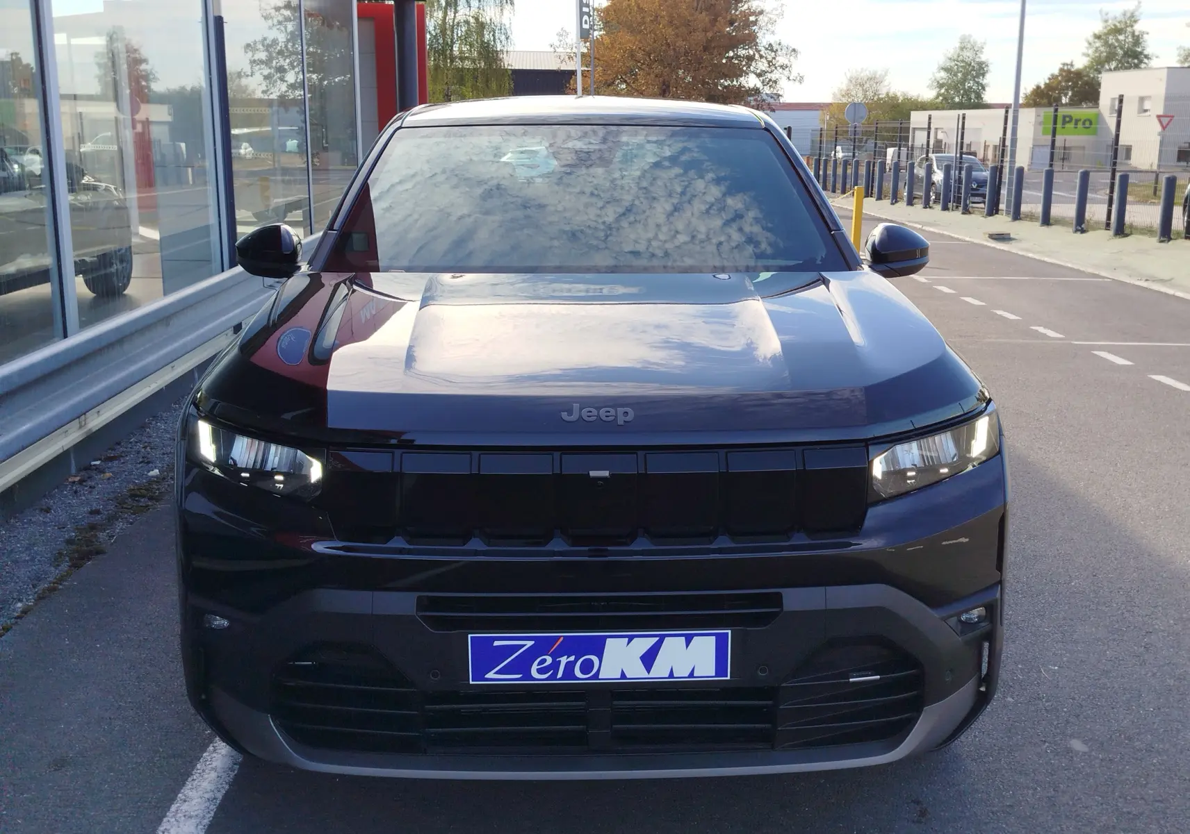 Vue frontale d’un Jeep Compass noir Vulcano métal avec calandre noire et phares LED allumés, stationné en extérieur.