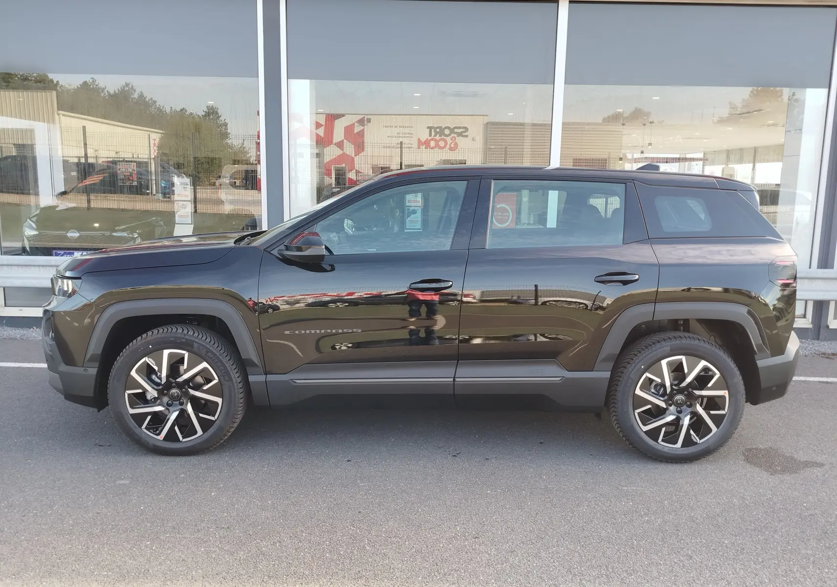 Profil latéral droit du Jeep Compass noir Vulcano métal 2026 avec jantes alliage et protections noires sur les passages de roues.