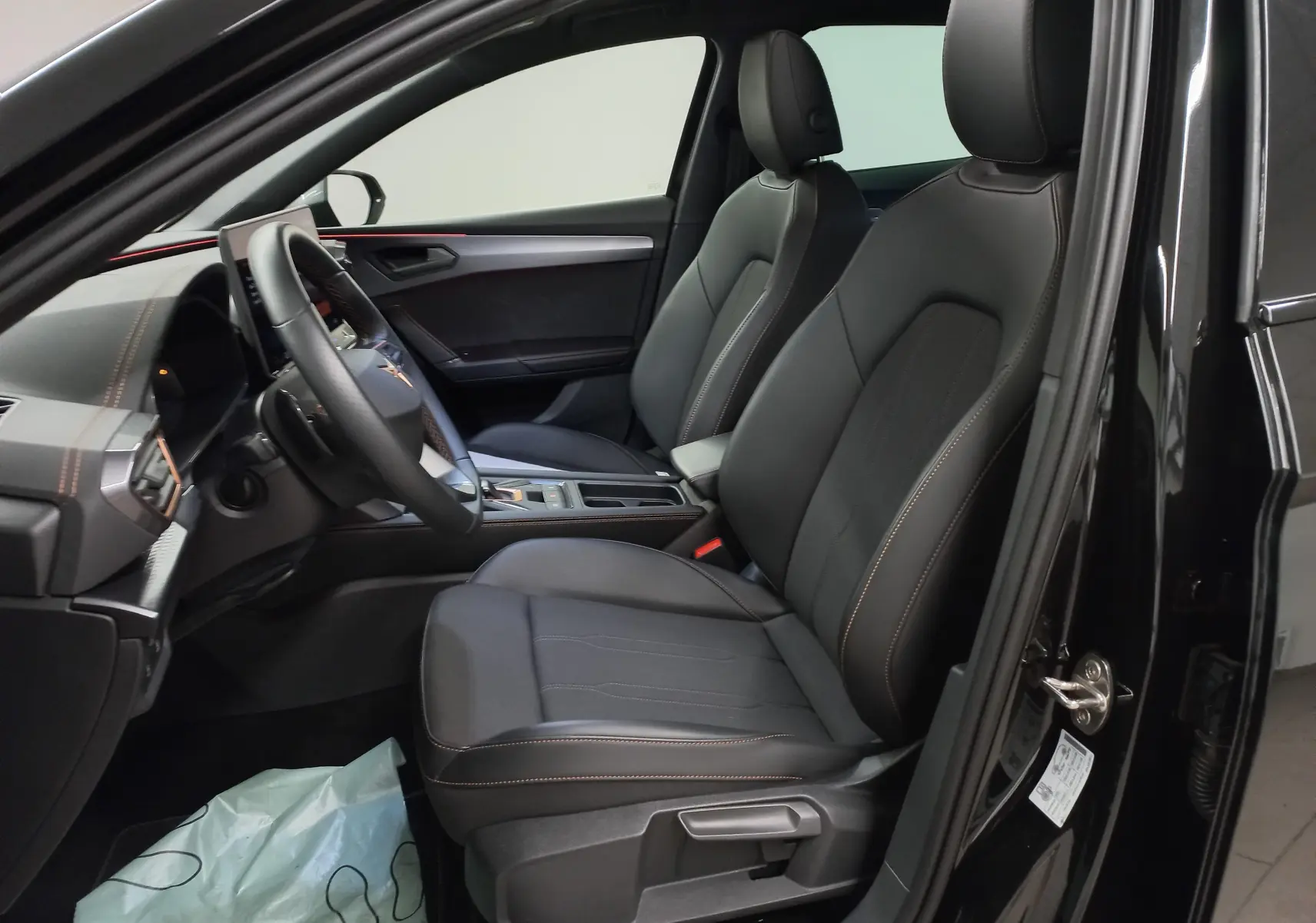 Vue intérieure côté conducteur de la CUPRA Leon 2025 noir minuit, sièges en cuir avec surpiqûres cuivrées et tableau de bord moderne.