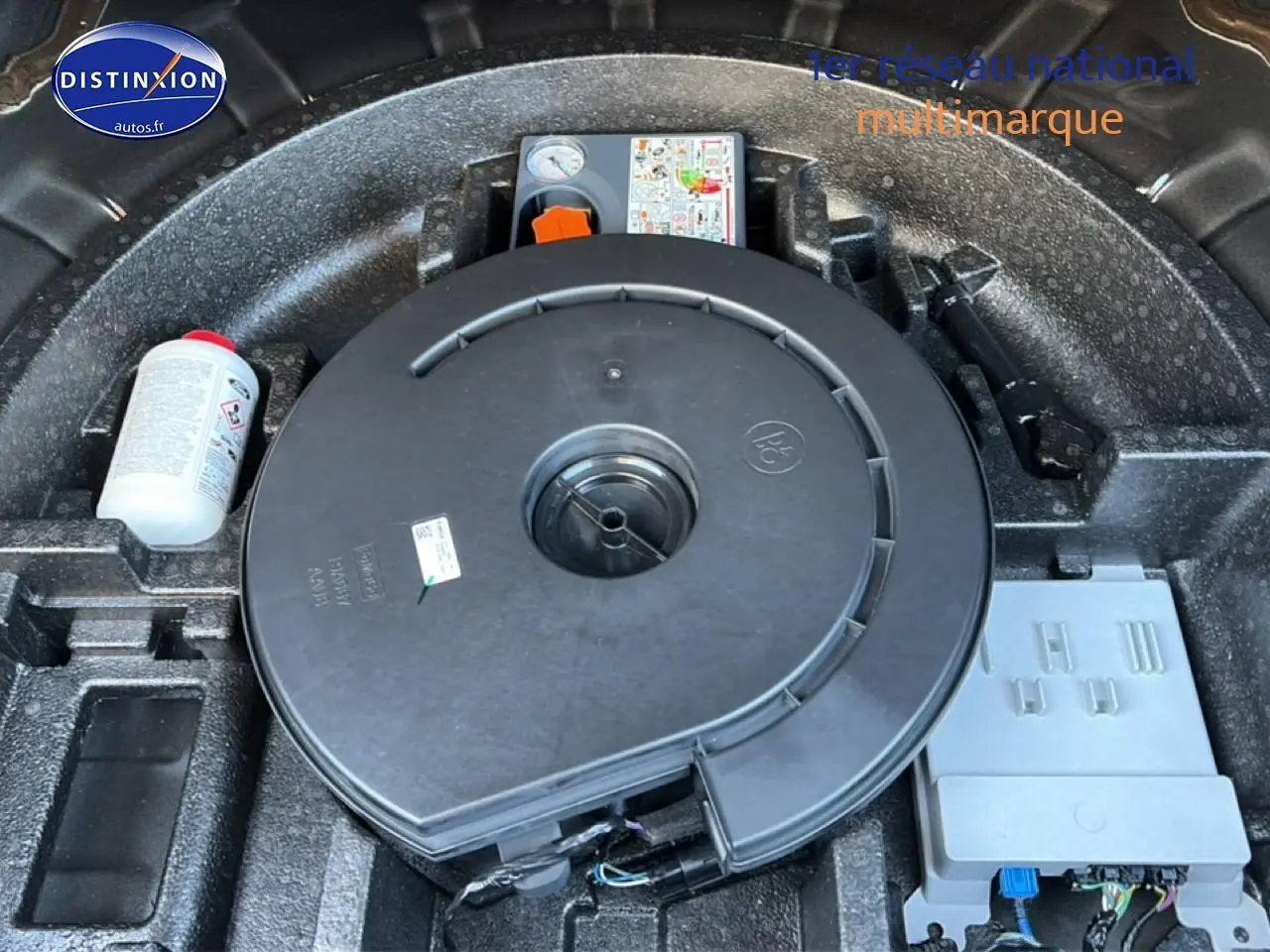 Vue rapprochée du coffre montrant la roue de secours et le kit de réparation sur fond noir.