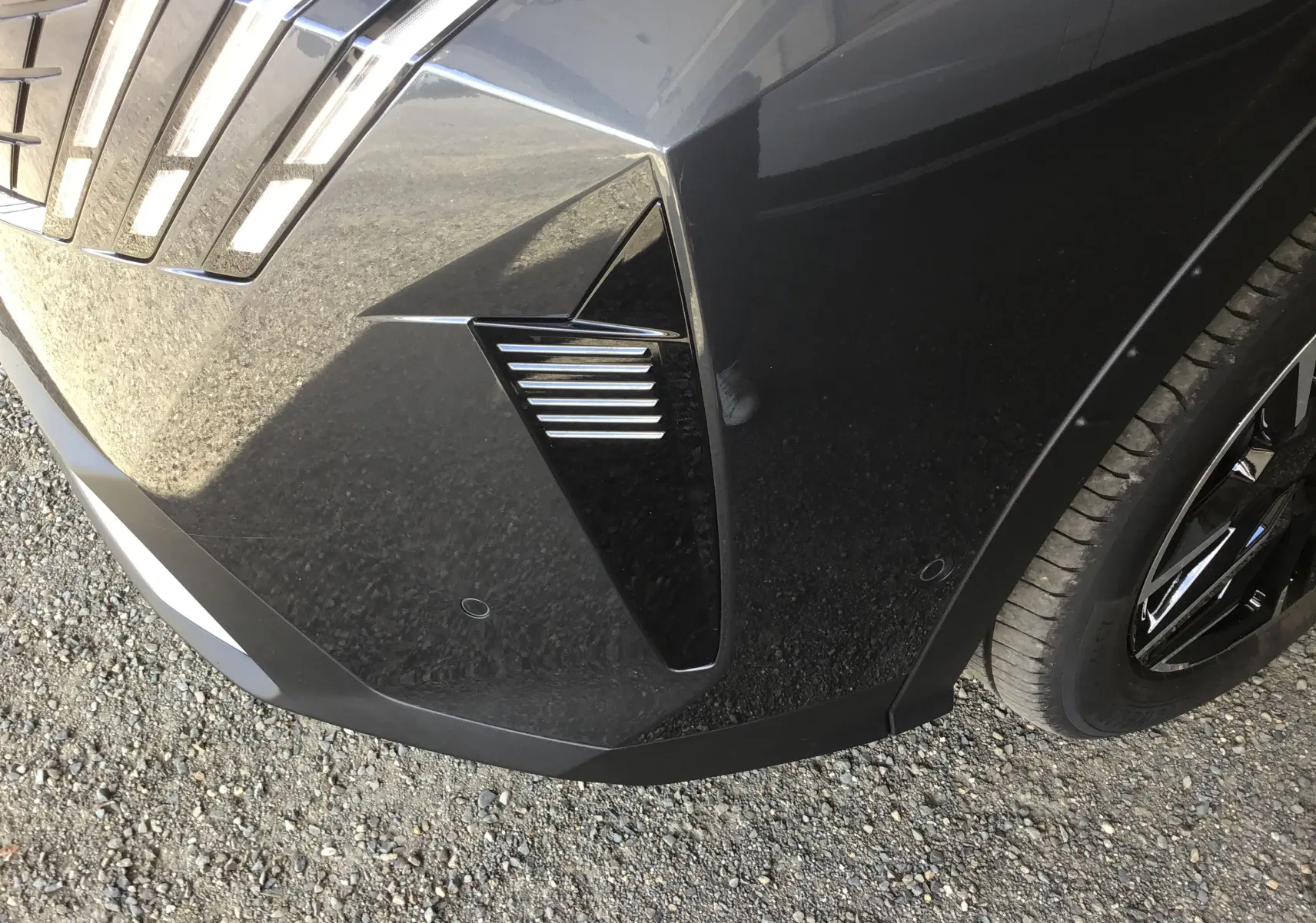 Gros plan sur l'avant droit gris titane du Peugeot 3008 1.2 Hybrid 145 Allure avec détails de la calandre et jante noire.