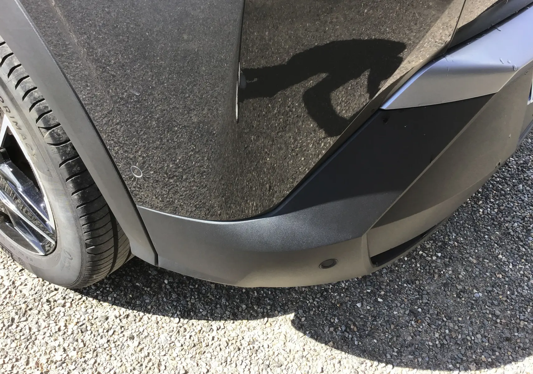 Gros plan sur l'angle avant droit du Peugeot 3008 gris titane, mettant en valeur le pare-chocs et la roue.