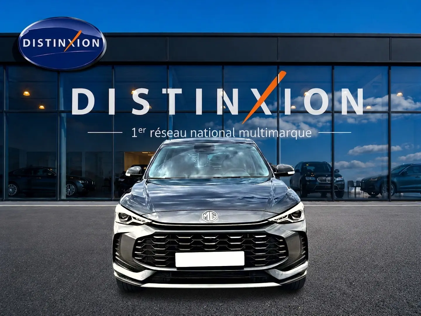 Vue de face du MG ZS 1.5 hybrid Camden grey avec calandre noire et phares LED devant un showroom Distinxion.