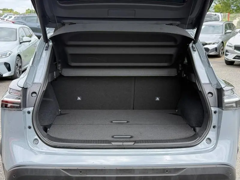 Coffre ouvert vue arrière d'un Nissan Qashqai 2025 gris Argile, montrant l'espace de chargement plat et le cache-bagages relevé.