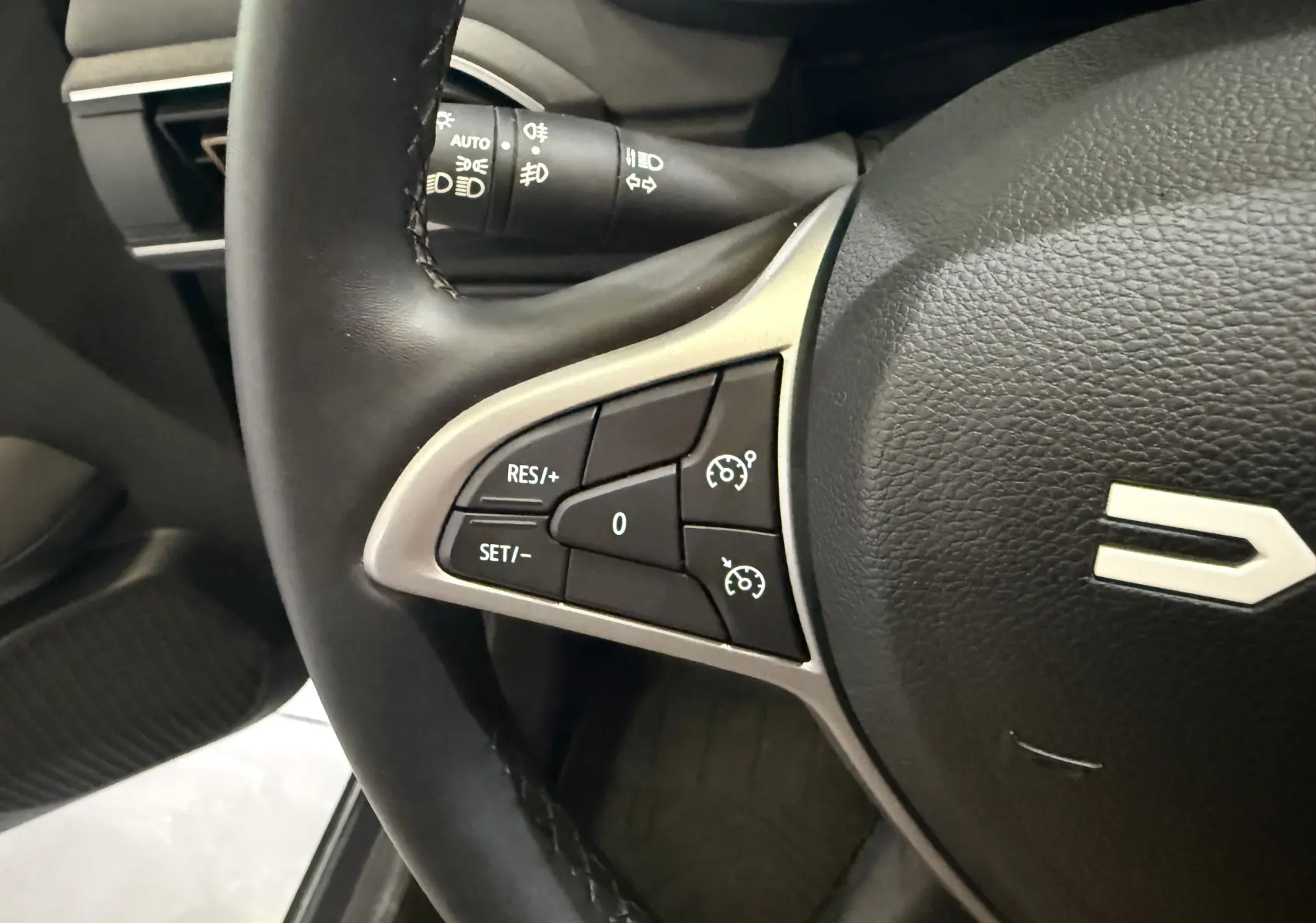 Gros plan sur les commandes de régulateur de vitesse à gauche du volant noir du Dacia Jogger Hybrid 140 Extreme 2023.