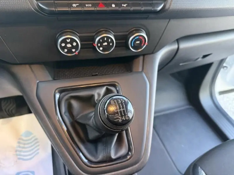 Gros plan sur le levier de vitesse manuel du Renault Kangoo blanc 2022, avec commandes de climatisation visibles en arrière-plan.