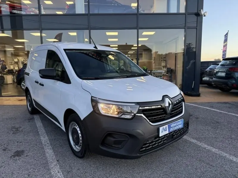 Renault Kangoo Van DCI blanc vu en 3/4 avant droit, avec calandre noire et feu avant allumé, stationné devant un showroom.