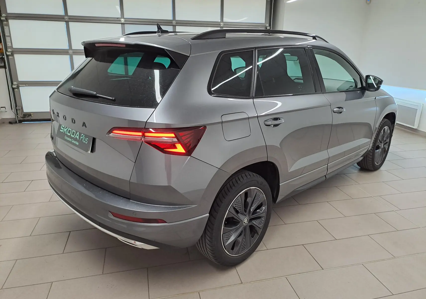 Vue 3/4 arrière droite du Skoda Karoq gris graphite métallisé avec feux arrière allumés dans un garage.