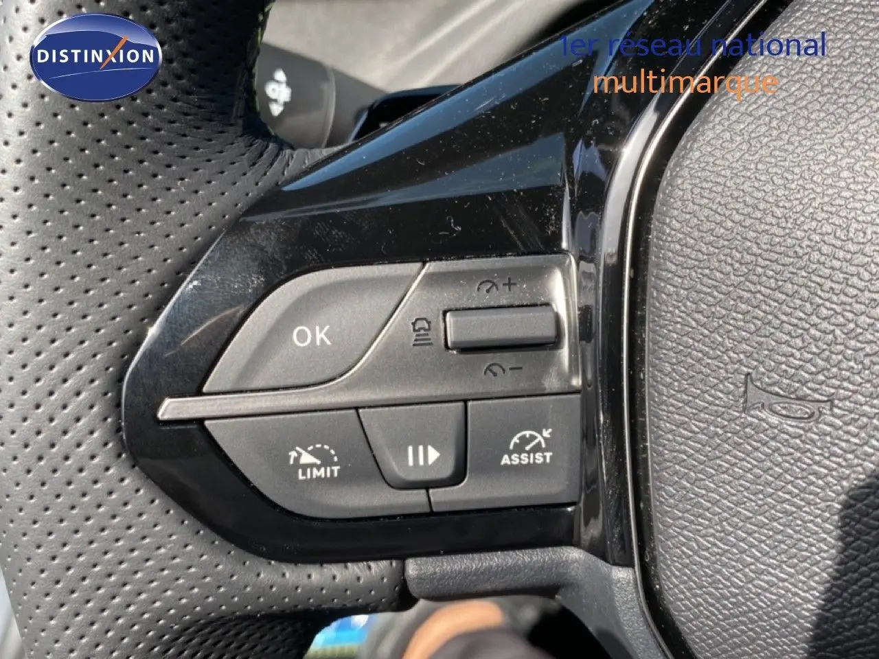 Gros plan sur les commandes de régulateur de vitesse au volant noir perforé d’une Peugeot 308 Hybrid blanche.