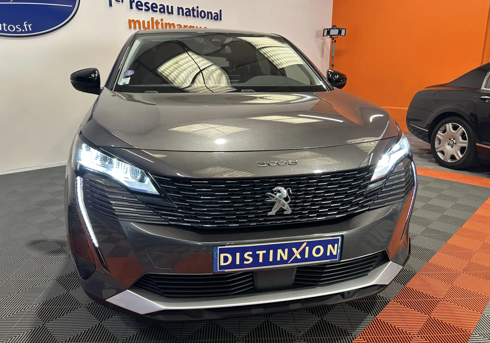 Vue avant d'un Peugeot 3008 gris Platinium avec phares LED allumés et calandre noire distinctive en showroom.