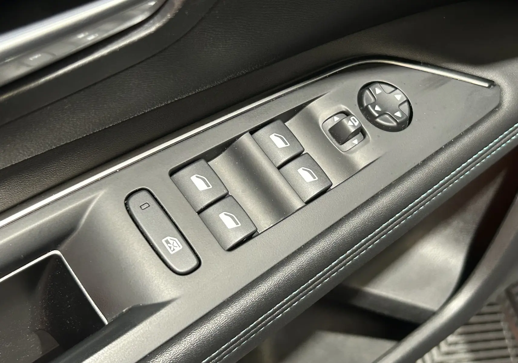 Gros plan sur les commandes de lève-vitres et réglage des rétroviseurs côté conducteur, finition noire avec surpiqûres bleues.