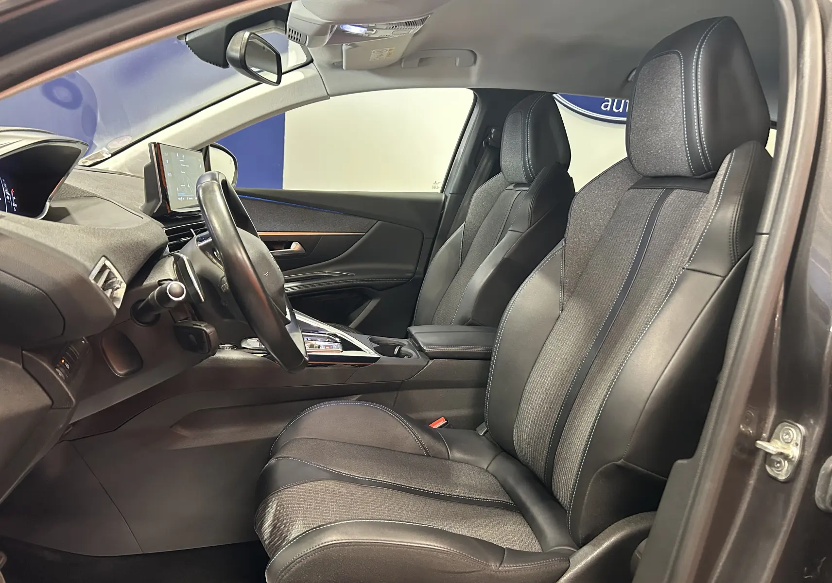 Vue intérieure côté conducteur du Peugeot 3008 Gris Platinium 2022, sièges en cuir et tissu avec surpiqûres bleues.