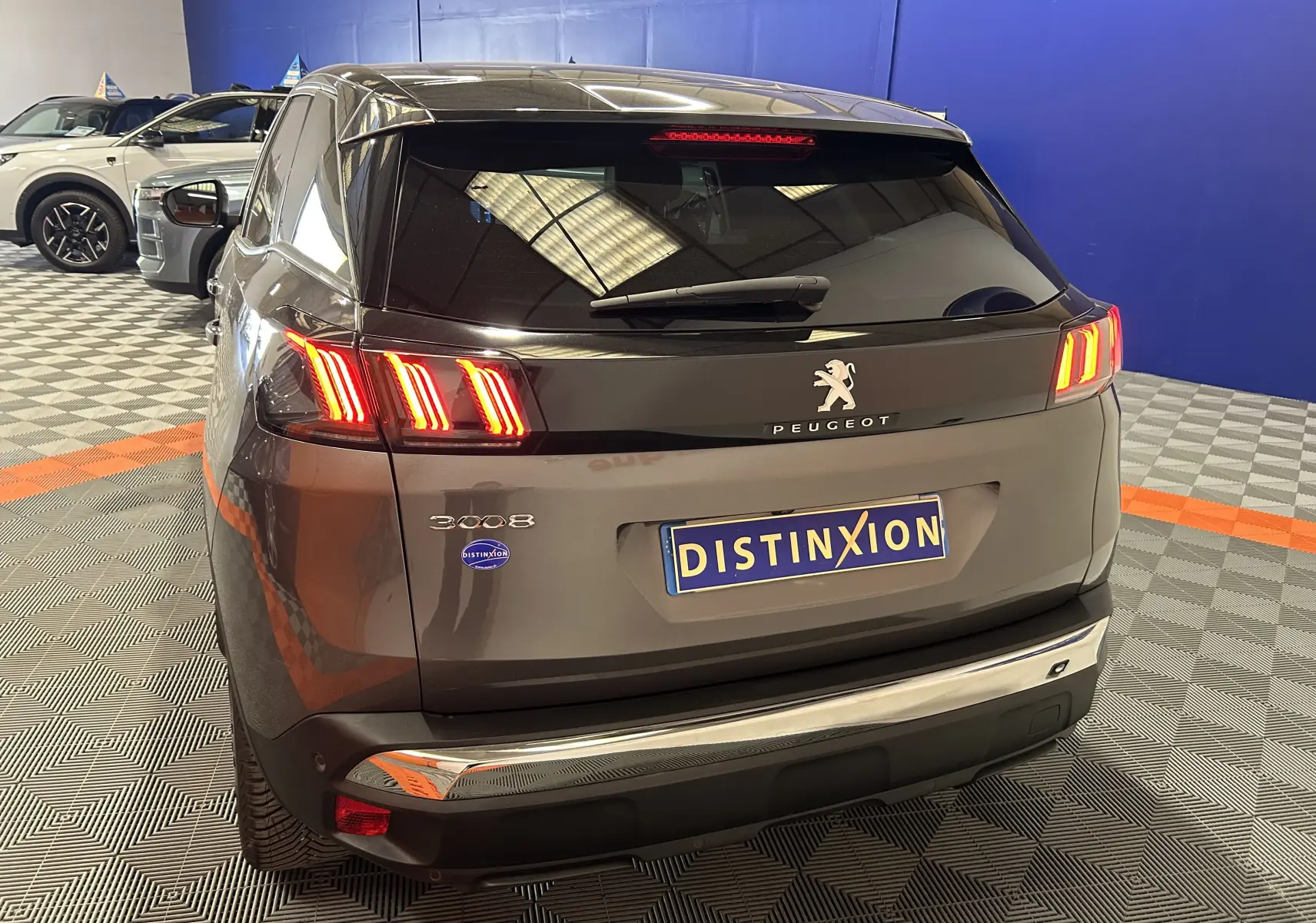 Vue 3/4 arrière droite du Peugeot 3008 gris Platinium avec feux arrière allumés et logo Distinxion visible.