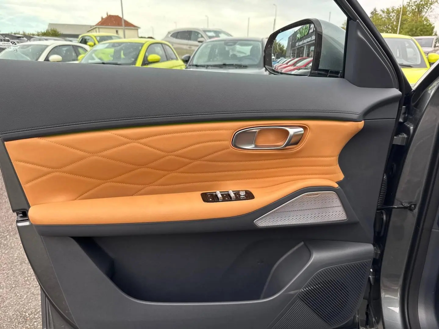 Vue intérieure côté gauche de la porte d’une Geely STARRAY 1.5 EM-i 262ch Max+ en Volcanic Grey avec garniture cuir marron et haut-parleur Harman Kardon.