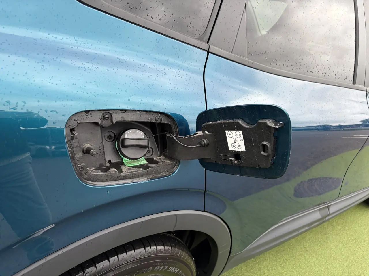 Gros plan sur la trappe à carburant côté gauche d’un Renault Arkana bleu Zanzibar métal, avec bouchon ouvert.