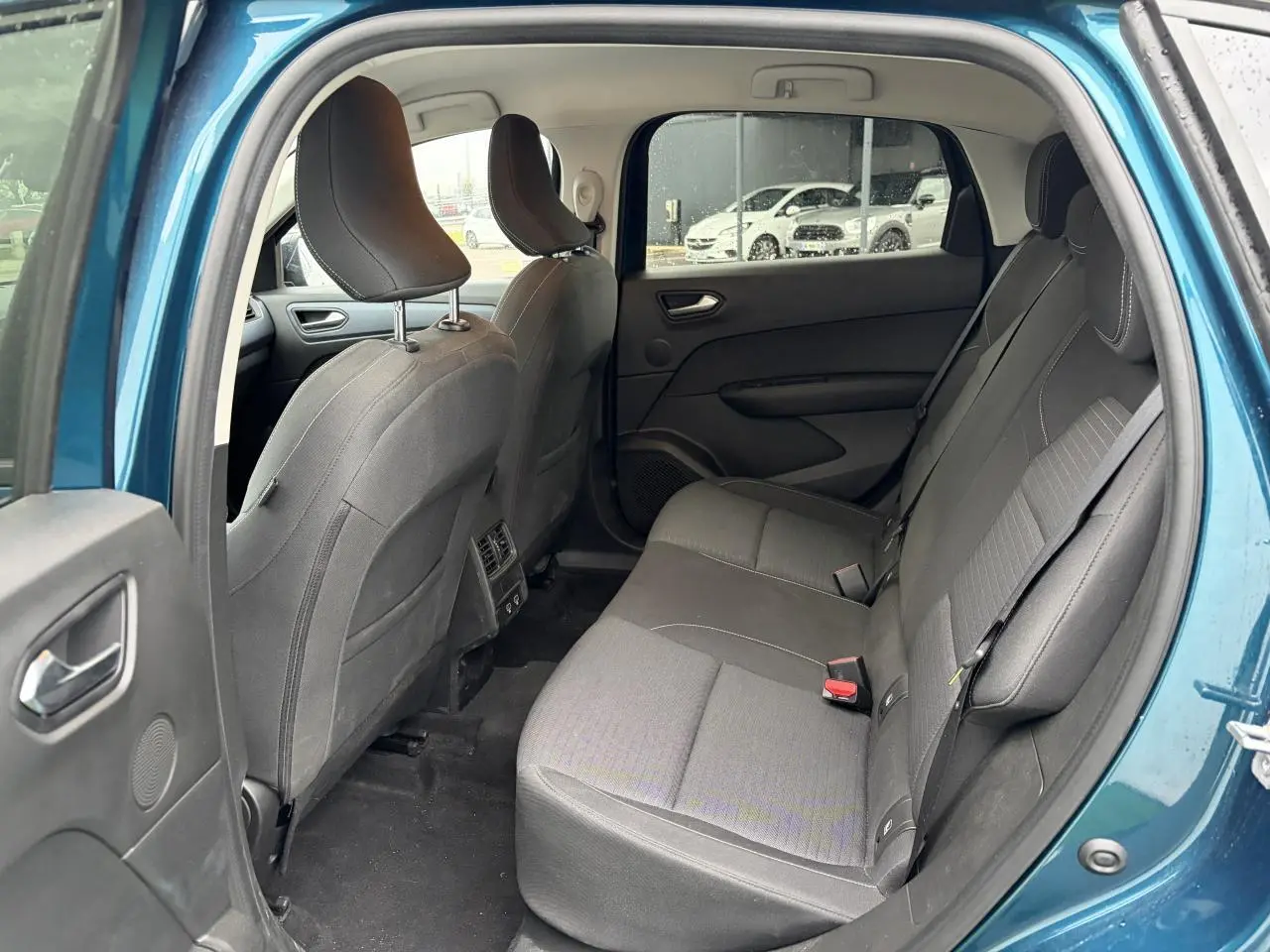 Vue intérieure arrière côté gauche du Renault Arkana bleu Zanzibar, montrant les sièges arrière gris et les portes ouvertes.