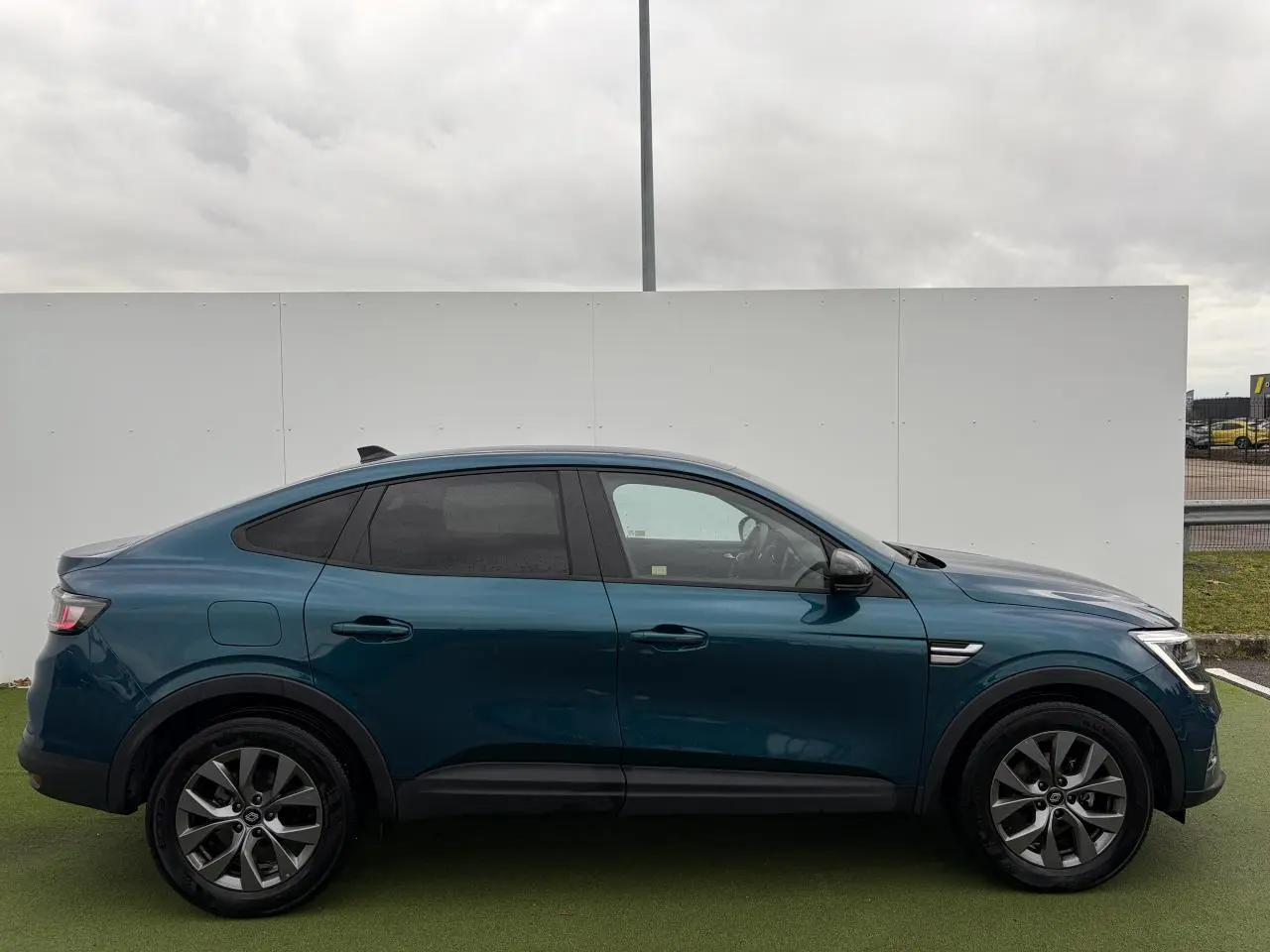 Vue de profil côté gauche d'un Renault Arkana 2025 bleu Zanzibar métal avec vitres surteintées et jantes alliage grises.