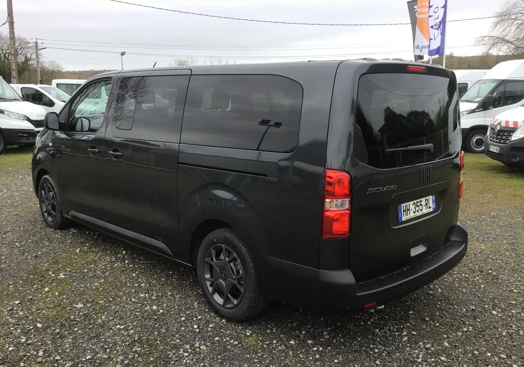 Vue 3/4 arrière droite d’un FIAT Scudo Combi gris titane avec vitres latérales surteintées et hayon fermé sur un parking extérieur.