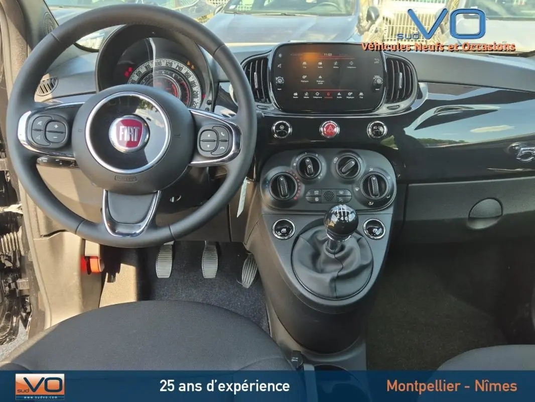 Vue intérieure avant de la Fiat 500C noire 2024, avec volant multifonction, tableau de bord digital et levier de vitesse manuel.