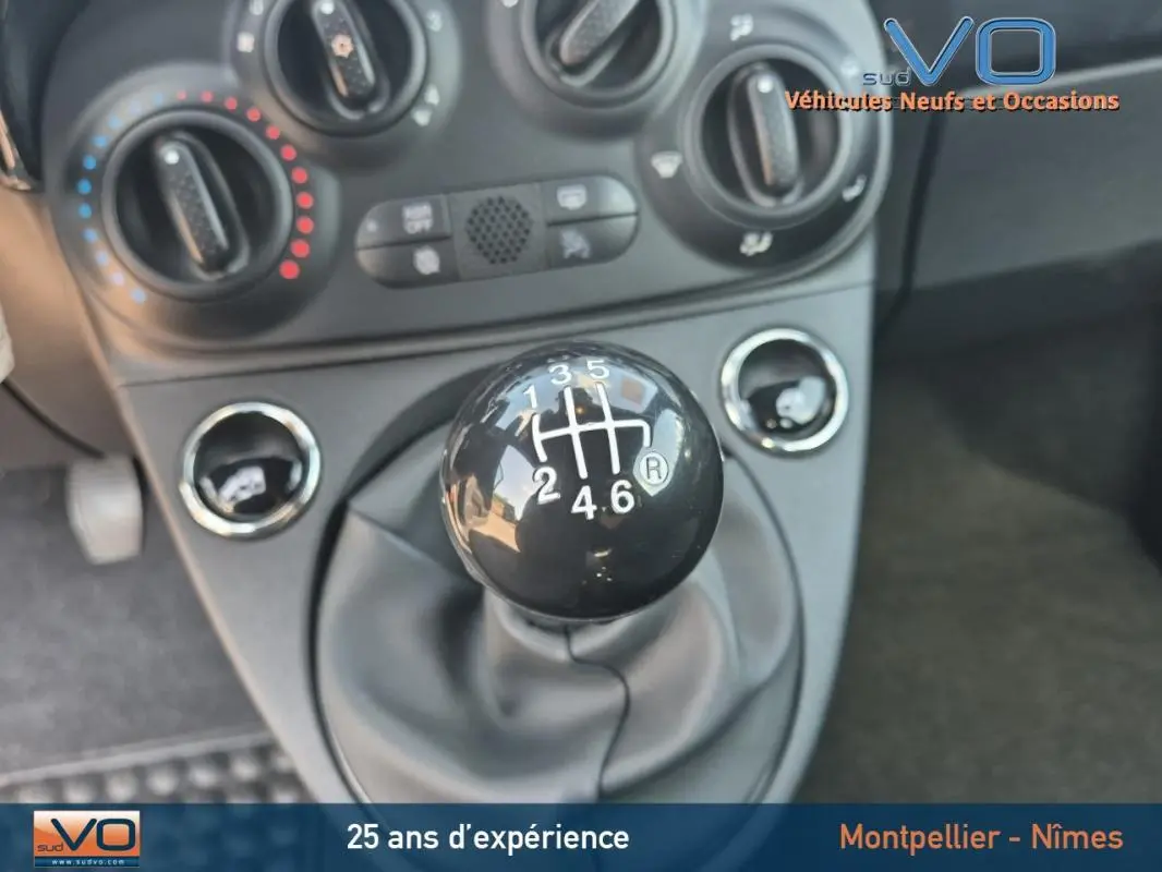 Gros plan sur le levier de vitesses manuel noir de la FIAT 500C 2024, avec commandes de climatisation en arrière-plan.