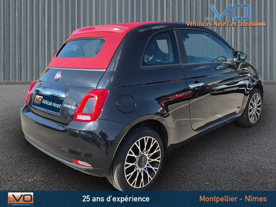Vue 3/4 arrière droite de la FIAT 500C noire avec toit rouge et jantes alliage 15 pouces, version hybride 2024.