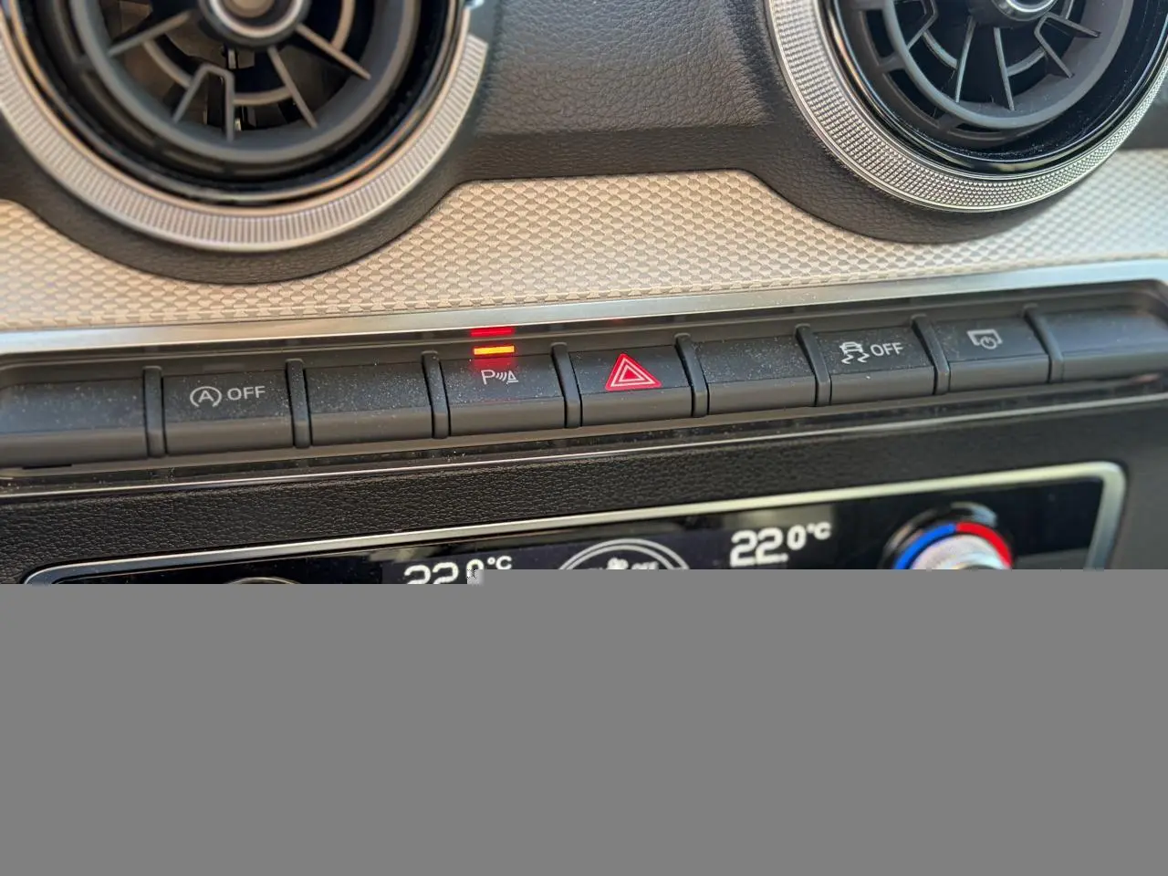 Gros plan sur la console centrale de l'Audi Q2 35 TFSI 2024, boutons de contrôle avec témoin lumineux rouge actif.