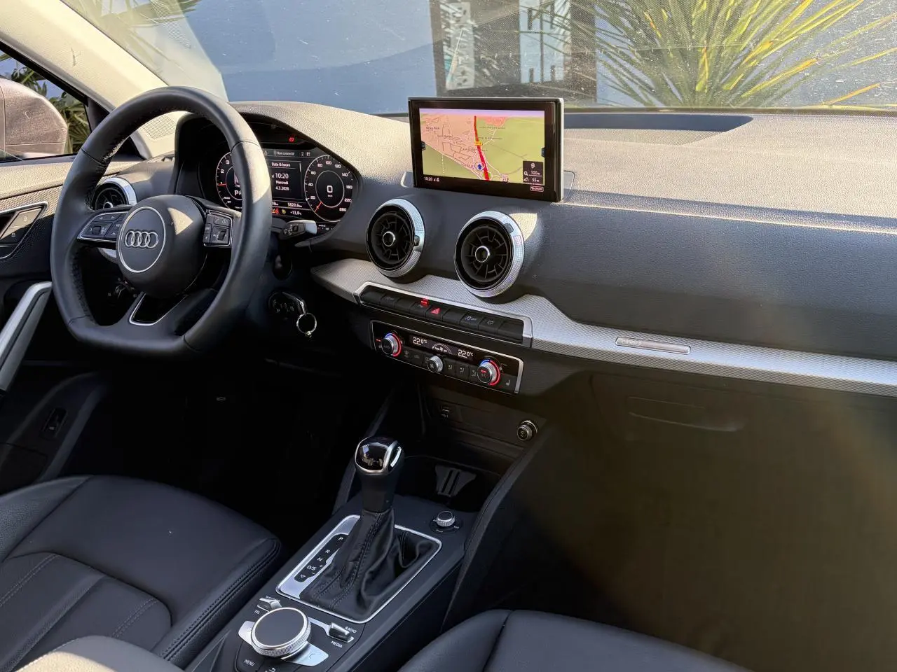 Vue intérieure côté conducteur de l'Audi Q2 2024, tableau de bord avec écran GPS et volant cuir multifonction.