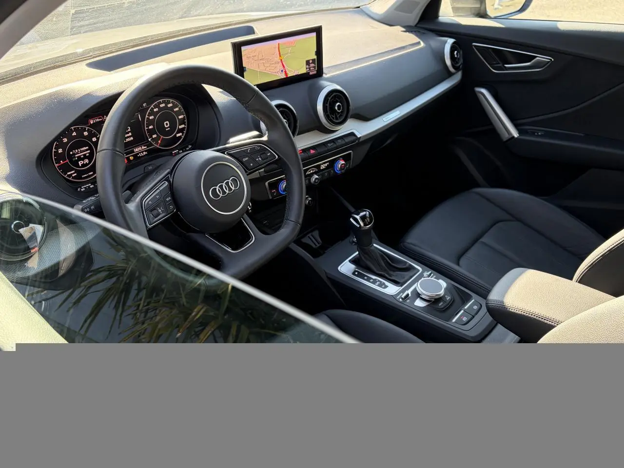 Vue intérieure côté conducteur de l'Audi Q2 35 TFSI S-Line 2024, volant cuir, écran GPS et tableau de bord numérique.