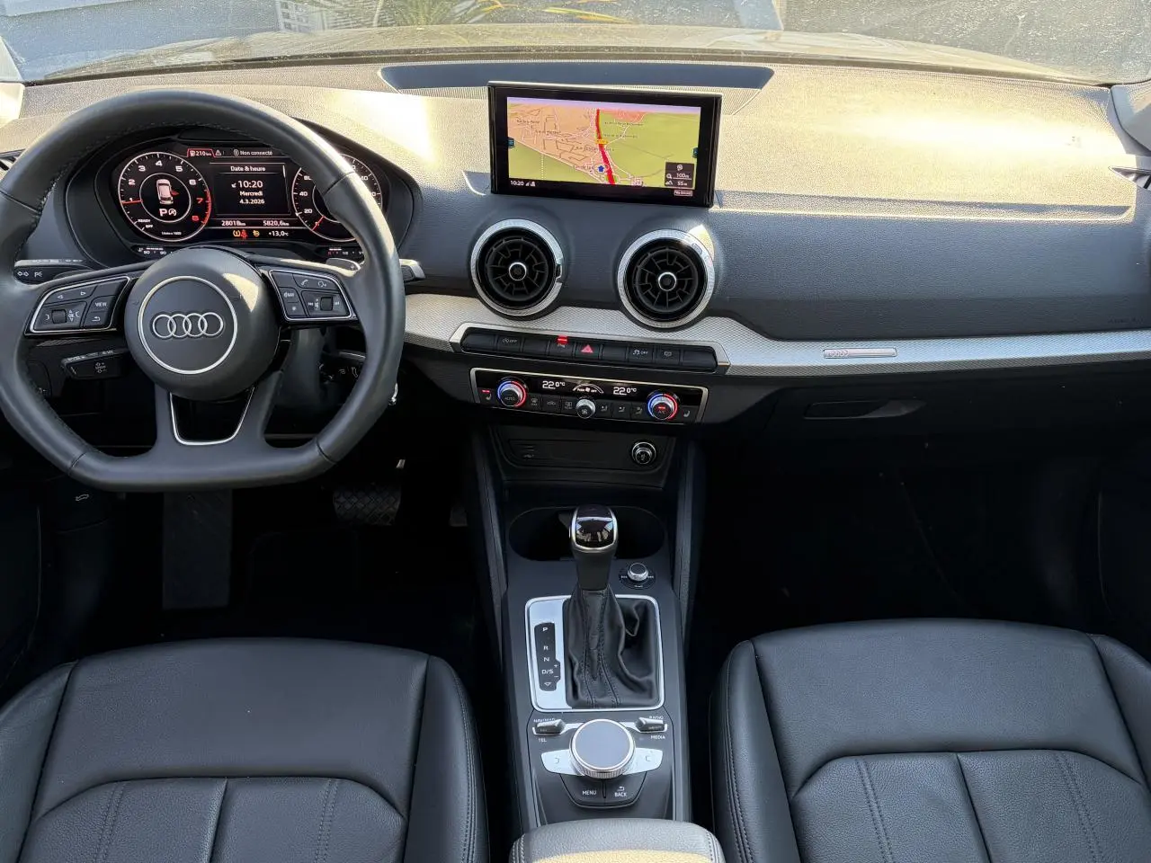 Vue intérieure avant de l'Audi Q2 35 TFSI S-Line 2024, tableau de bord noir avec écran GPS et volant multifonction cuir.