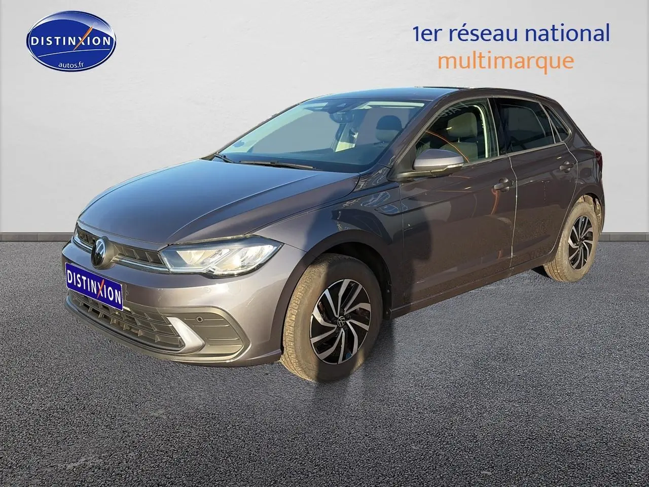 Volkswagen Polo gris vue 3/4 avant droit avec jantes alu et phares LED allumés sur fond clair.