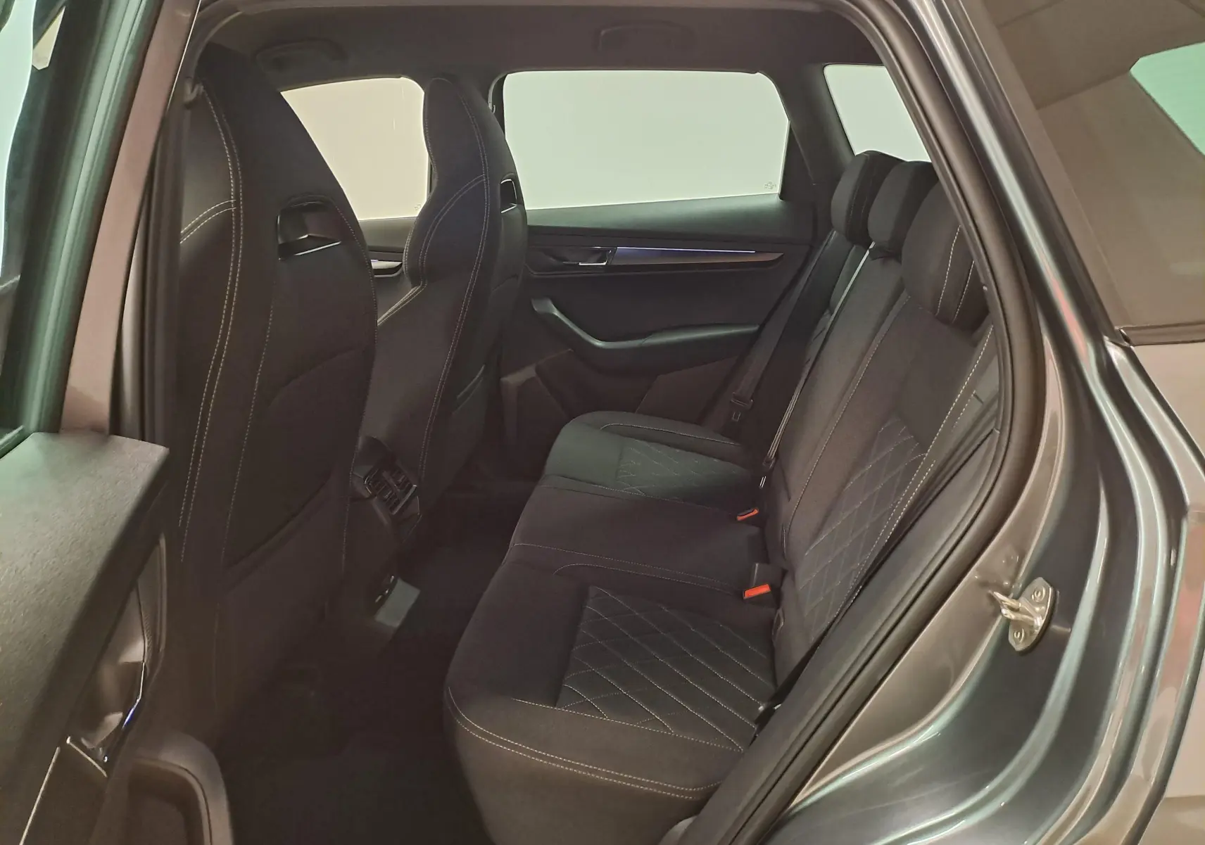 Vue intérieure côté droit des sièges arrière noirs avec surpiqûres blanches du Skoda Karoq gris graphite 2025.