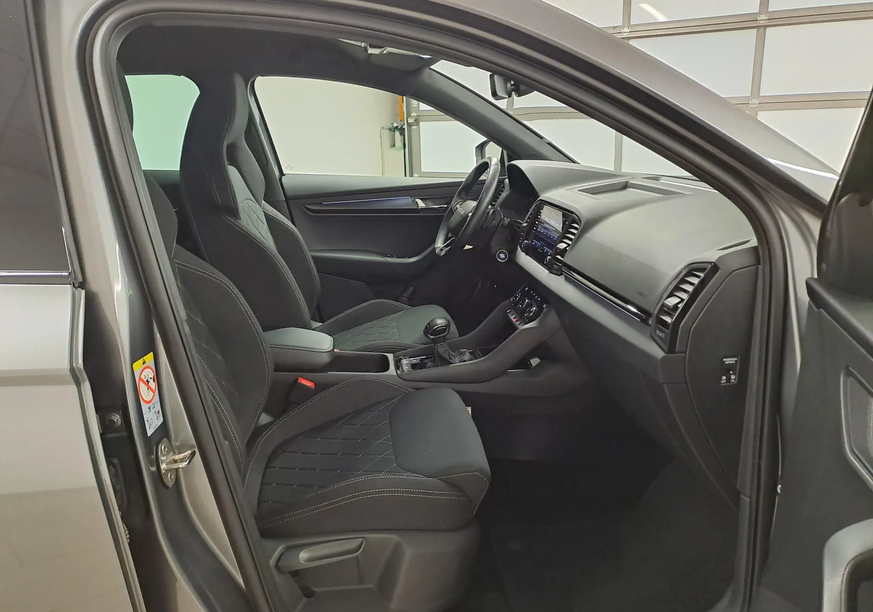 Vue intérieure côté conducteur du Skoda Karoq gris graphite 2025, sièges sport noirs et tableau de bord moderne.
