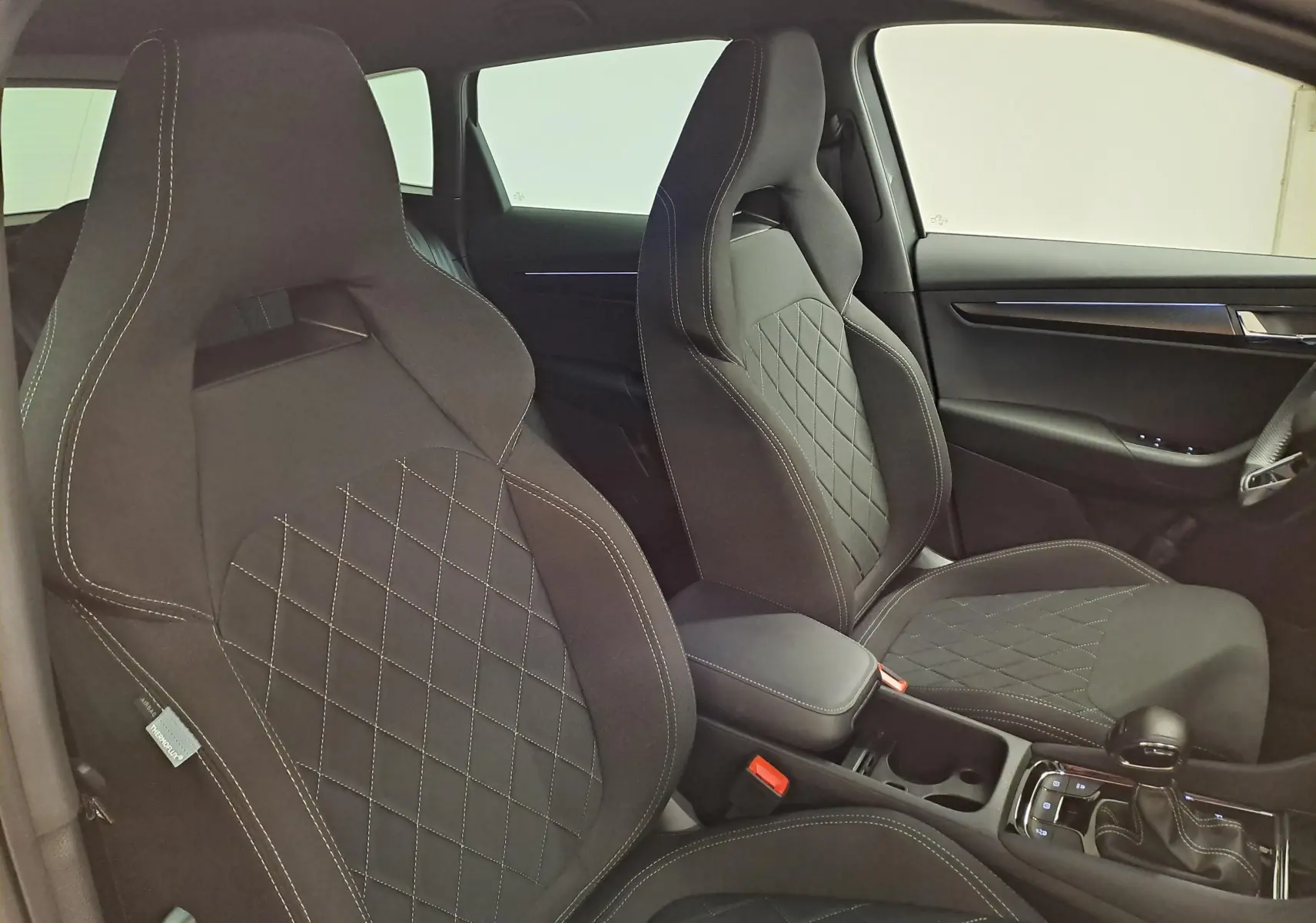 Vue intérieure des sièges avant noirs avec surpiqûres blanches et console centrale du Skoda Karoq 2.0 TDI 150 DSG7 Sportline.