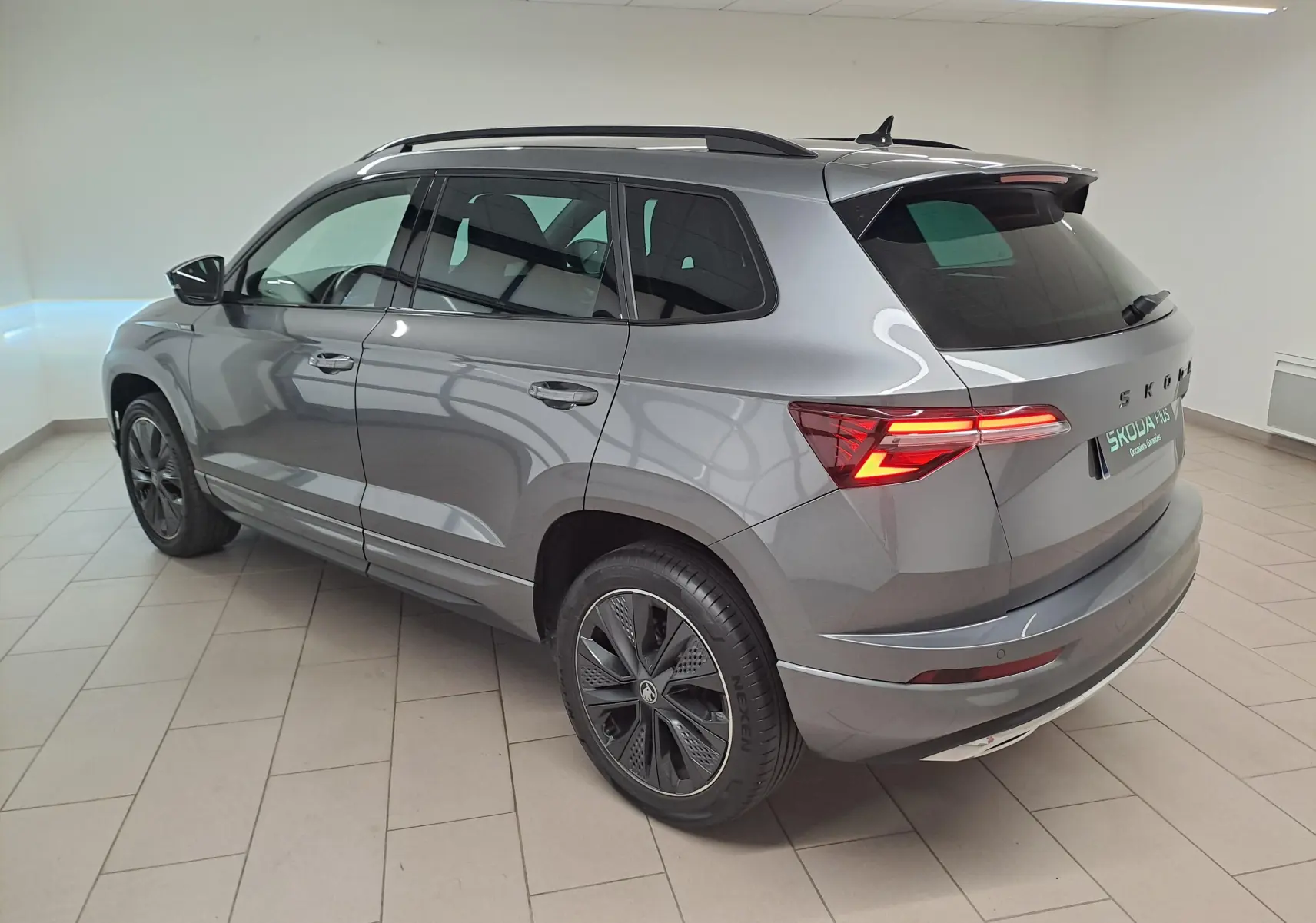 Vue 3/4 arrière droite du Skoda Karoq gris graphite 2025 avec feux allumés et jantes noires sportline.