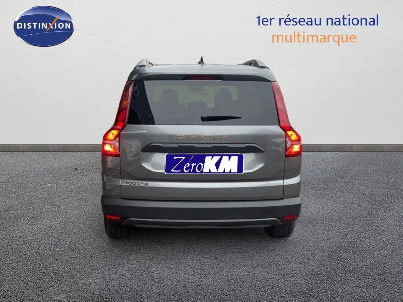 Vue arrière d'un Dacia Jogger gris schiste métal avec feux allumés sur un sol gris uniforme.
