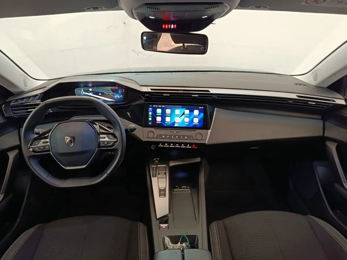 Vue intérieure avant de la Peugeot 308 2023, tableau de bord noir avec écran tactile central et volant cuir multifonctions.