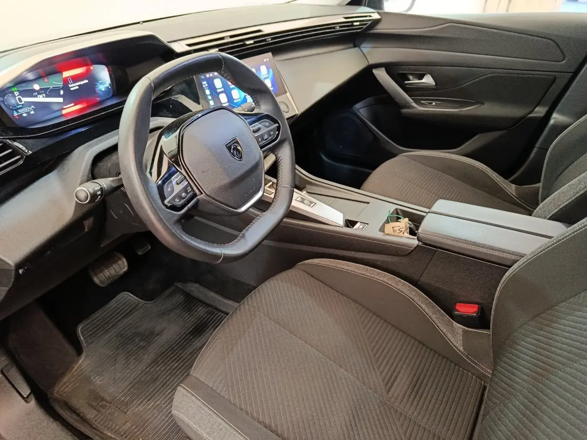 Vue intérieure côté conducteur de la Peugeot 308 2023, avec volant cuir, tableau de bord digital et sièges noirs.