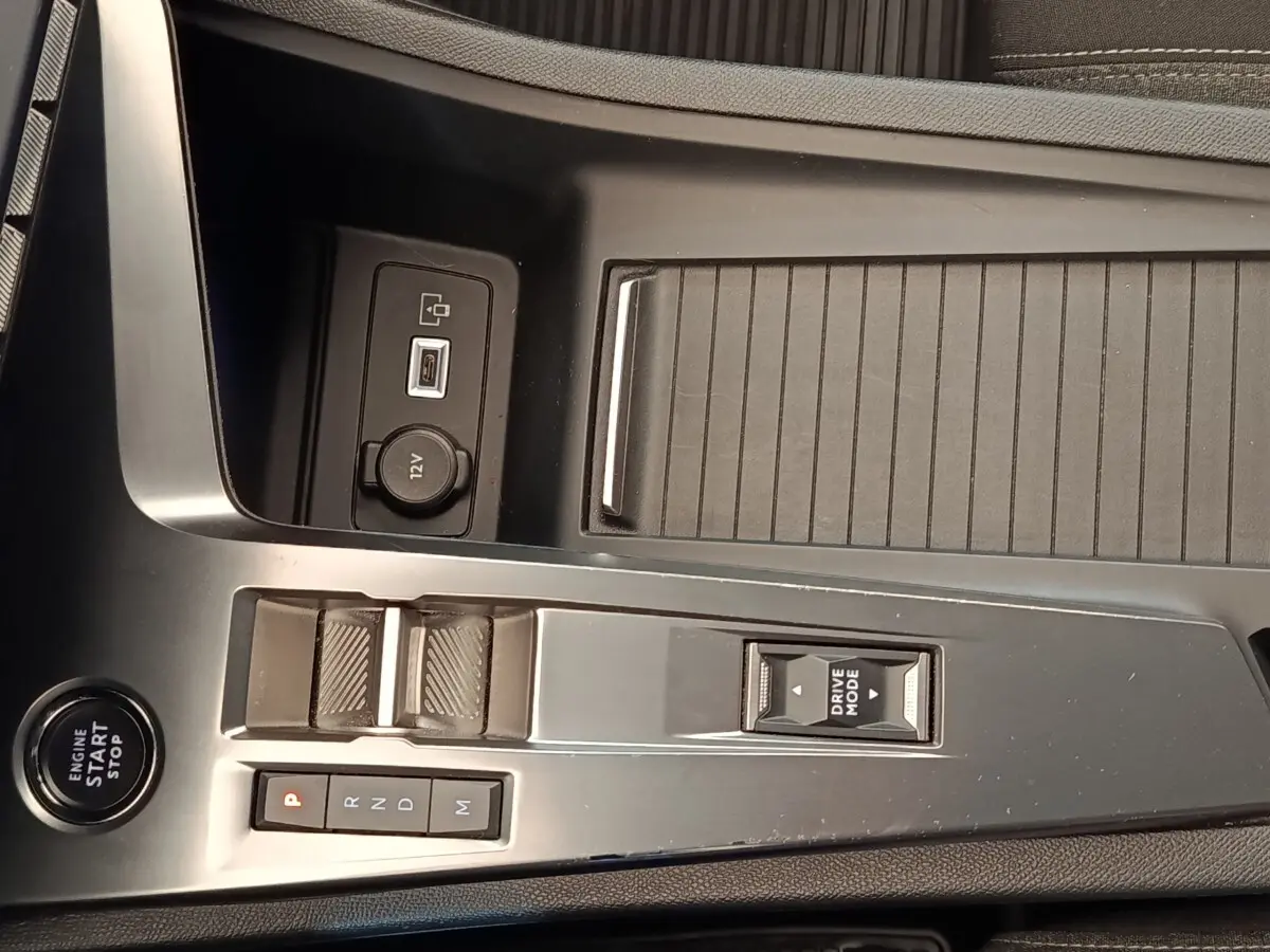 Vue rapprochée de la console centrale noire du Peugeot 308 2023 avec bouton start, sélecteur de mode et prise 12V.