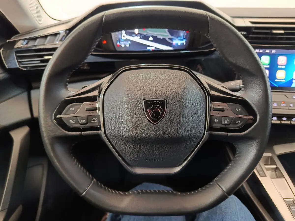 Vue rapprochée du volant cuir noir de la Peugeot 308 2023 avec commandes multifonctions et tableau de bord digital.