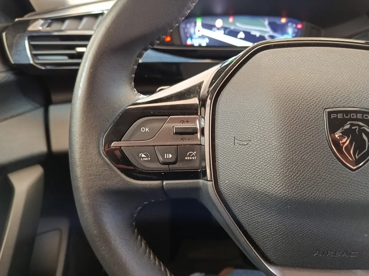 Gros plan sur le volant cuir noir de la Peugeot 308 2023 avec commandes multifonctions et logo lion central.