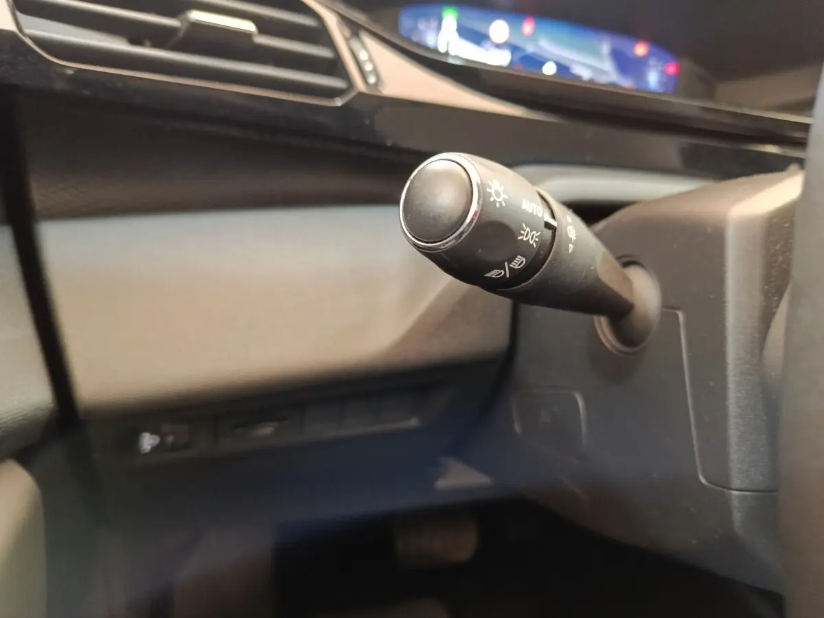 Gros plan sur la commande de phares noire à gauche du volant dans l’habitacle gris foncé du Peugeot 308 2023.