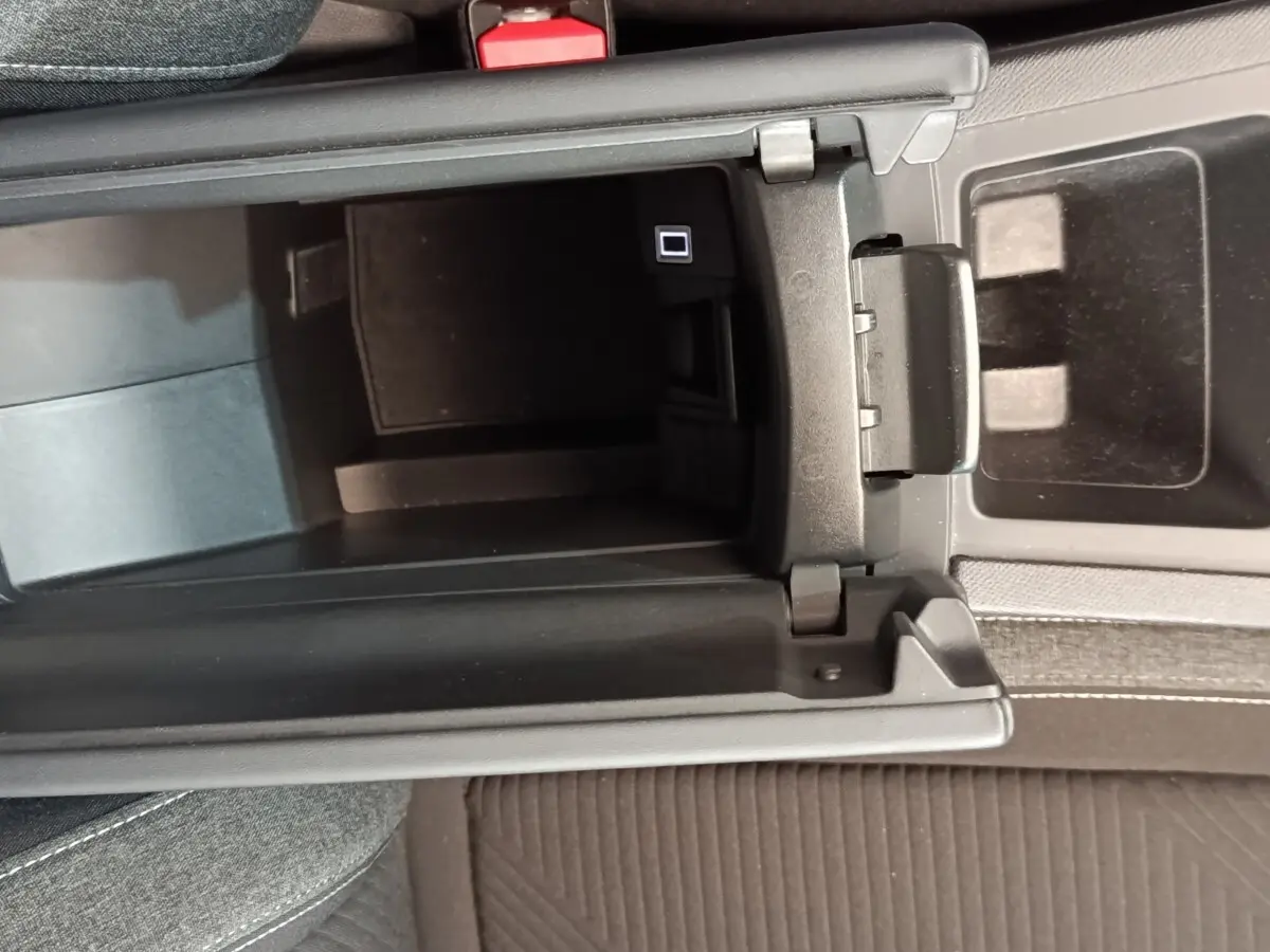 Vue plongeante sur le rangement central noir ouvert de la Peugeot 308 2023 essence, avec console et siège tissu gris.