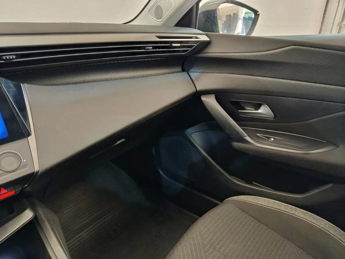 Intérieur côté passager de la Peugeot 308 2023, tableau de bord et porte en noir avec détails texturés.